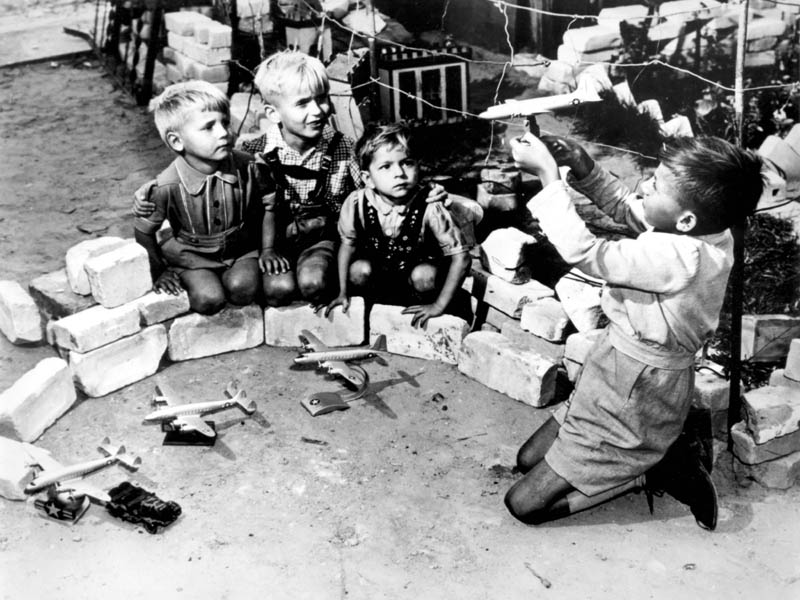 "OPERATION VITTLES" (Berlin Airlift)  Berlin youngsters who live near the Tempelhof Air Force Base, where the U.S. Air Force transport planes unload their airlift supplies, play at a game called "Luftbrucke" (air bridge).  They use model American planes which are sold in German toy shops throughout the western sector of Berlin. (Wikipedia)